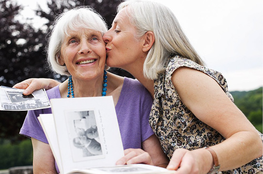 A female caregiver kisses an elderly woman on the cheek.